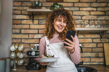 curly hair woman eat fresh salad while use mobile phone and smile