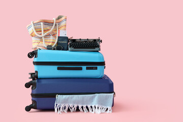 Suitcases with vintage typewriter and beach accessories on pink background