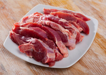 White plate with sliced fresh raw turkey thigh on wooden background..