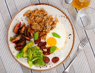 Appetizing hunting sausages and scrambled eggs served with basil, buckwheat, sun-dried tomatoes and avocados on a plate on the tablecloth