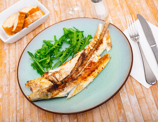 Fresh baked fish sea bass with arugula on a ceramic plate in a restaurant