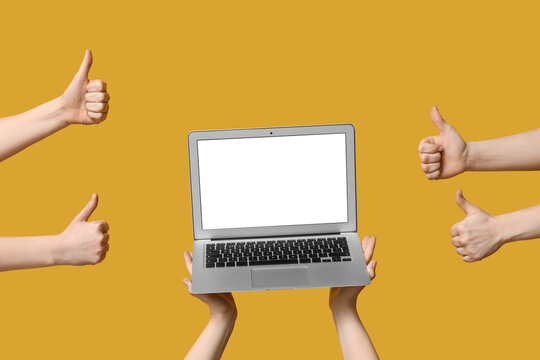 Female hands with blank laptop showing thumbs-up on yellow background