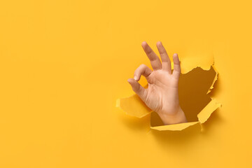 Female hand showing OK visible through hole in yellow paper