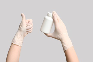 Doctor's hands with pill bottle showing thumb-up on light background