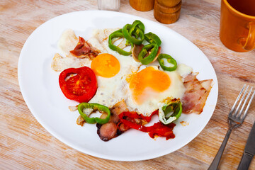 Appetizing scrambled eggs with bacon and vegetables served on plate