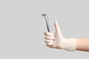 Dentist's hand with tools showing thumb-up on light background