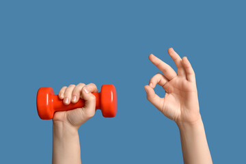 Female hands with dumbbell showing OK on blue background