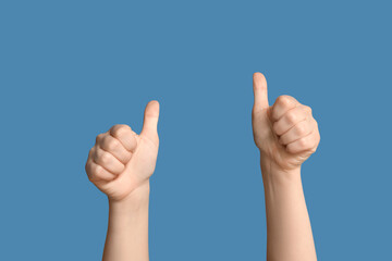 Female hands showing thumbs-up on blue background