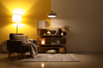 Interior of dark living room with armchair, bookshelf and glowing lamps