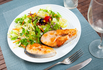 Two delicious fried salmon steaks served with salad of fresh vegetables and greens, corn and olives. Healthy food concept..