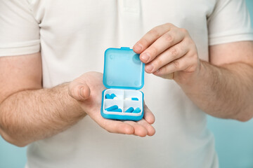Young man with pill box on blue background, closeup