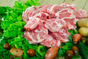 Raw lamb meat on wooden cutting board on background with fresh vegetables and greens