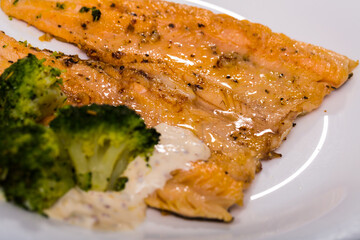 Plate of baked trout fillet served with savory sauce and broccoli