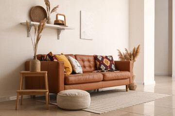 Brown leather sofa with soft pillows and pouf near white wall in living room