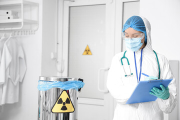 Medical worker in protective uniform and with container for radioactive waste in clinic
