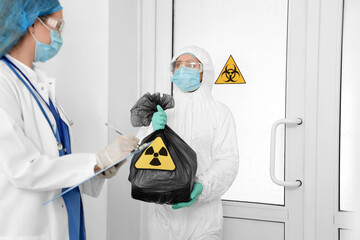 Workers in protective uniforms and with bag of radioactive waste in clinic