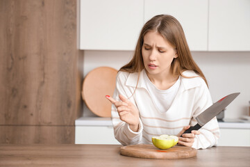 Troubled woman with injured finger after cutting of apple in kitchen