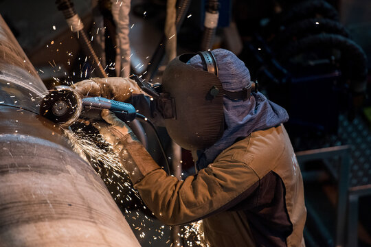 Industrial worker grinding metal pipe with sparks - Powered by Adobe