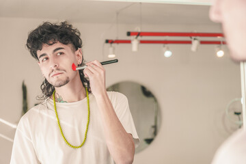 Young man applying makeup with brush in mirror: embracing diversity and inclusion