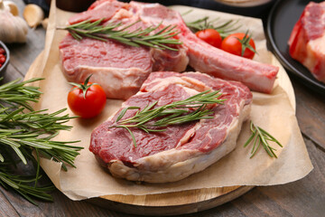 Pieces of raw beef, rosemary and tomatoes on wooden table, closeup