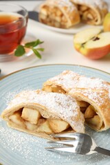 Pieces of tasty apple strudel with powdered sugar and fork on white table, closeup