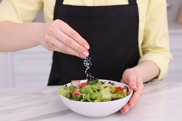 Woman salting tasty salad at white marble table indoors, closeup