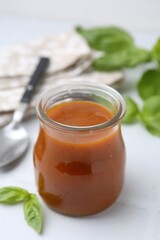 Tasty curry sauce in glass jar and basil on white tiled table, closeup