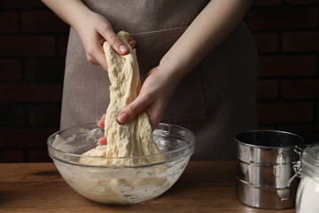 Woman kneading raw dough at wooden table, closeup