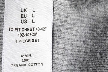 Clothing label with size and content information on grey garment, above view. Space for text