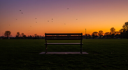 Obraz premium Park Bench Silhouette Against Vibrant Sunset Sky With Birds Flying