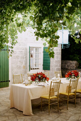 Festive table with bouquets of flowers stands in the courtyard of an old house under the green foliage of a tree