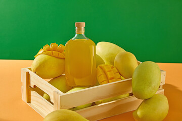A glass pitcher of fresh mango juice is placed between ripe and sliced mangoes. The smooth-skinned Alphonso mango fruit are stacked high, leaning against a wooden crate. Advertising photo.