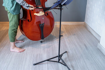 Barefoot Young musician practicing double bass with music stand at home