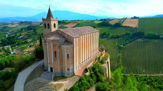 OFFIDA, ITALY - AUGUST 4, 2024: Aerial arcing truck left pan right shot of Chiesa di Santa Maria della Rocca. A hilltop sanctuary with an ancient crypt and authentic Renaissance frescoes
