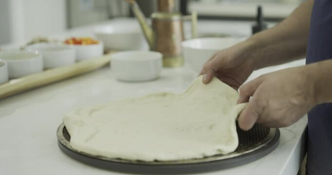 Closeup of person spreading sauce and cheese on pizza dough