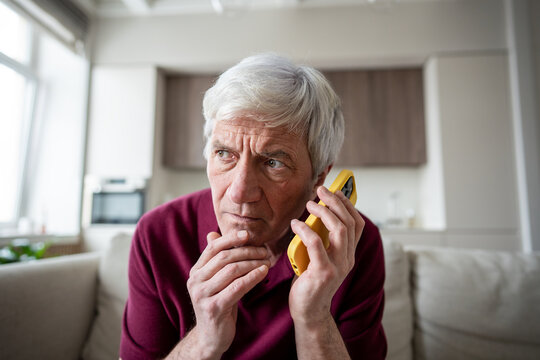 Tired distrust shocked retiree man in discomfort listening to unknown caller making dubious requests. Phone scam warning call, social engineering, elder fraud, telemarketing, call manipulation