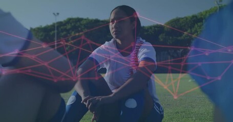 Female soccer player kneeling hugging knees on grass field, showing sports tech network overlay - Powered by Adobe
