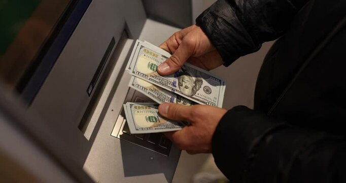 Man counts dollar bills standing near ATM machine on street at night. Customer withdraws cash money via banking automatic equipment outdoors