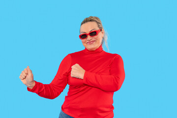 Naklejka premium Woman in red sweater dancing playfully against a bright blue background during a cheerful moment in a lively indoor setting