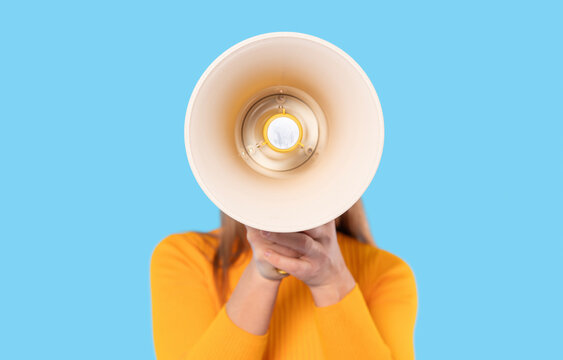 Woman holds megaphone in front of her against a bright blue background to amplify her voice during a public announcement