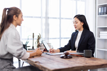 Two lawyers in suits discussing legal matters at a desk with a gavel, scales of justice, and a law book, symbolizing law and justice, justice and lawyer Business partnership meeting concept.

