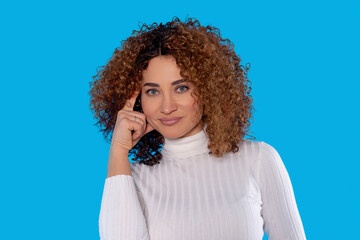 Beautiful woman with curly hair in white sweater poses with a thoughtful expression against a...