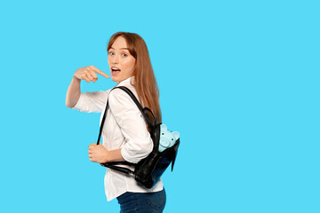 Woman with backpack and stuffed animal looking back at camera against a blue background during a casual indoor setting
