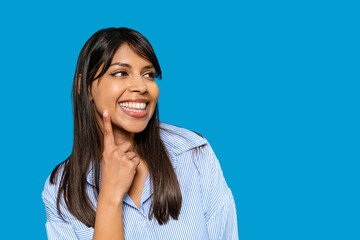 Smiling woman gestures thoughtfully against a bright blue background while wearing a striped shirt...