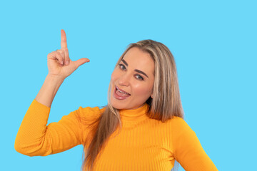 Smiling woman in a bright yellow sweater gestures playfully against a vivid blue background,...