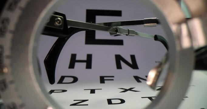 Vision testing glasses and Snellen eye chart with black letters rest neatly on desk. Pair of professional optometry glasses in examination room