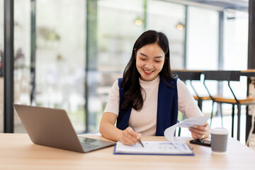 asian business woman sit at laptop holding papers, read received contract, agreement, legal documents smile feel satisfied, got good news. Loan repayment, career advance, success concept
