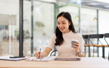 Obraz premium Smiling asian woman or accountant working with documents using calculator and tablet computer laptop at the office desk 