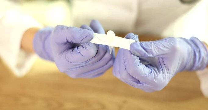 Doctor opens medical suppository and prepares for immediate use. Physician in protective gloves tears protective cover of treatment suppository