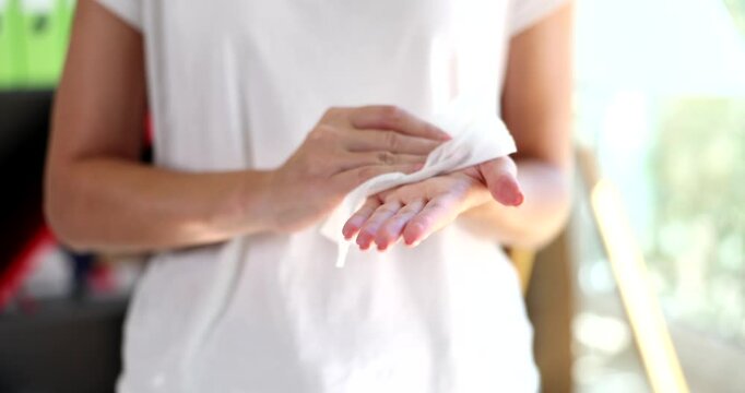 Woman in white t-shirt wipes hands with sanitary napkin. Lady with nails painted light pink cleans hands with soft material standing in light room